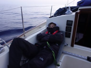 person sleeping in a cockpit of a sailing boat