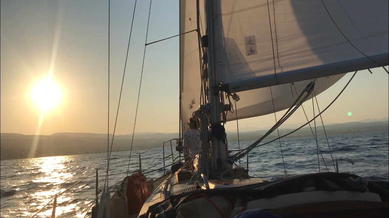 girl sat on the bow of a sailing boat at sunset